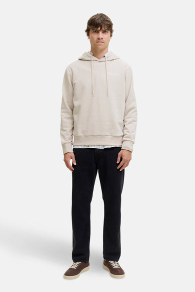 Sweater écru avec capuche JJREBEL, avec des cordons de serrage et porté sur un chemisier à carreaux et des jeans noirs.