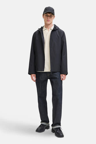 Pull beige à col V de PREMIUM BLUE par JACK & JONES, porté sous un manteau bleu marine, avec des jeans foncés et des chaussures noires.