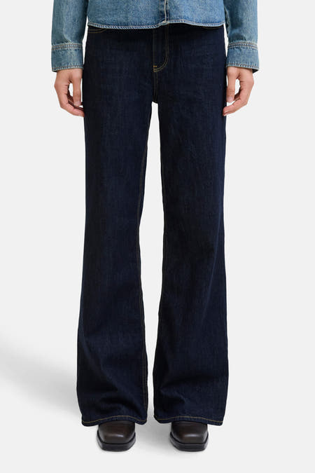 Jean flare bleu marine de JJXX avec des surpiqures jaunes, associé à une veste en denim sur un fond blanc.