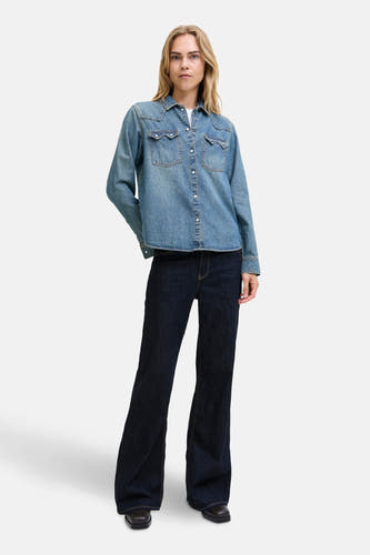 Jean flare bleu marine de JJXX, associé à une chemise en denim et des chaussures marron.