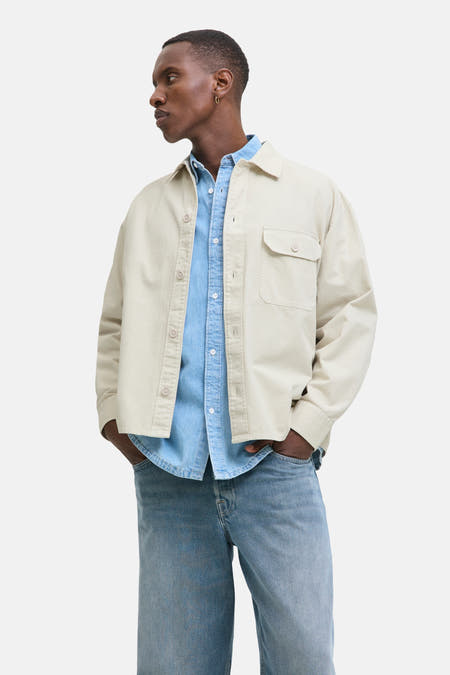 Chemise beige de PREMIUM BLUE par JACK & JONES, portée sur une chemise denim bleue avec des jeans.