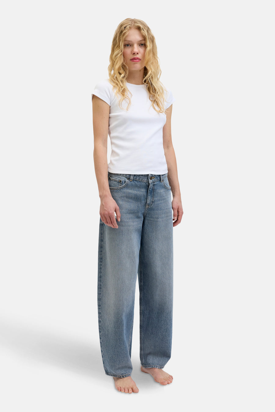 Jean en denim bleu moyen avec des jambes larges de JJXX, porté avec un T-shirt blanc, sur un fond blanc.