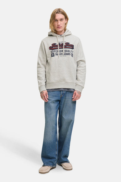 Pull-over blanc avec capuche d'ORIGINALS BY JACK & JONES, avec une impression graphique sur la poitrine, associé à des jeans bleus et des chaussures beige.