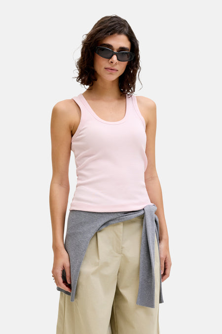 Débardeur côtelé rose de JJXX, porté par un mannequin avec un pull gris, un pantalon beige et des lunettes de soleil.