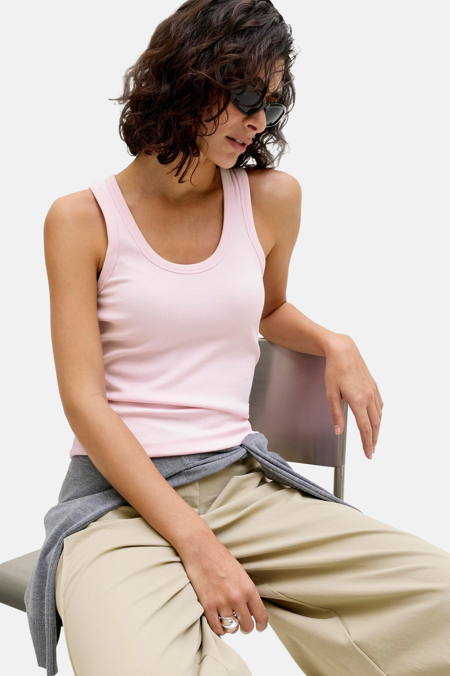 Débardeur côtelé rose de JJXX, porté par un mannequin avec des lunettes de soleil, un pantalon beige et un gilet gris autour de la taille.