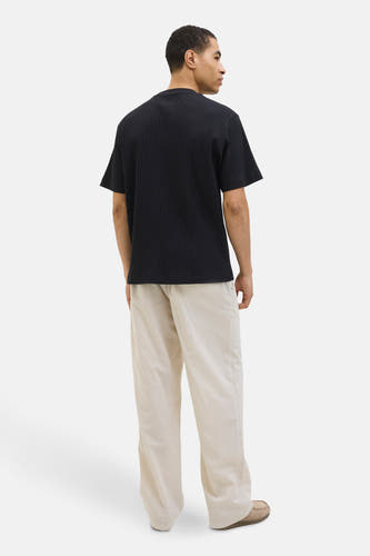 T-shirt noir à manches courtes de CORE BY JACK & JONES, avec un tissu côtelé vertical, porté avec des pantalons beige.
