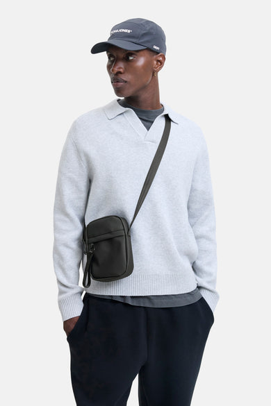 Sac à dos noir d'ACCESSORIES BY JACK & JONES, avec une sangle d'épaule ajustable, porté par un modèle avec un pull gris et un chapeau.