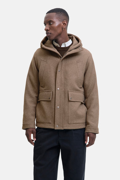 Manteau long beige de PREMIUM par JACK & JONES, avec capuche et poches, porté avec un chemisier et une veste.