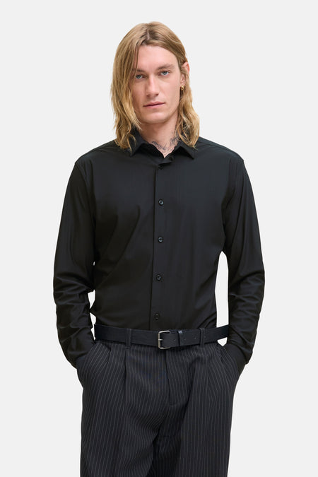 Chemise noire à manches longues de PREMIUM by JACK & JONES, avec fermeture boutonnée et portée avec un pantalon rayé.