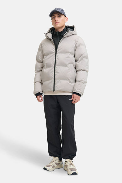 Manteau court écru de CORE BY JACK & JONES, avec capuche et fermeture éclair noire, associé à un pantalon de sport noir et des baskets beige.