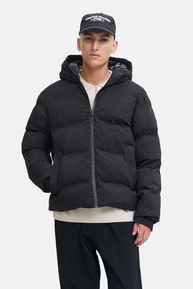 Manteau court noir de CORE BY JACK & JONES, avec capuche et un modèle avec une main dans la poche.