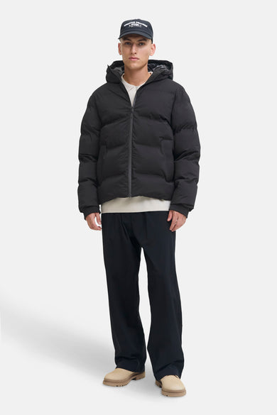 Manteau court noir de CORE BY JACK & JONES, avec capuche, associé à une chemise blanche, un pantalon noir et des chaussures beige.
