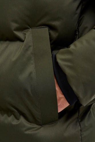 Manteau vert court de CORE BY JACK & JONES, avec une main dans la poche et des bordures de manches noires visibles.