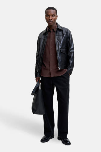 Marron, chemise à manches longues de PREMIUM BLUE par JACK & JONES, portée sous un manteau en cuir noir avec une sacque noire.