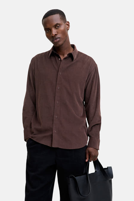 Chemise à manches longues marron de PREMIUM BLUE par JACK & JONES, portée avec un pantalon noir et une valise.