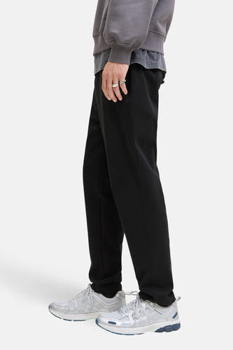 Pantalon noir de JACK & JONES JEANS INTELLIGENCE, avec des baskets argentées et un pull gris, vue de côté.