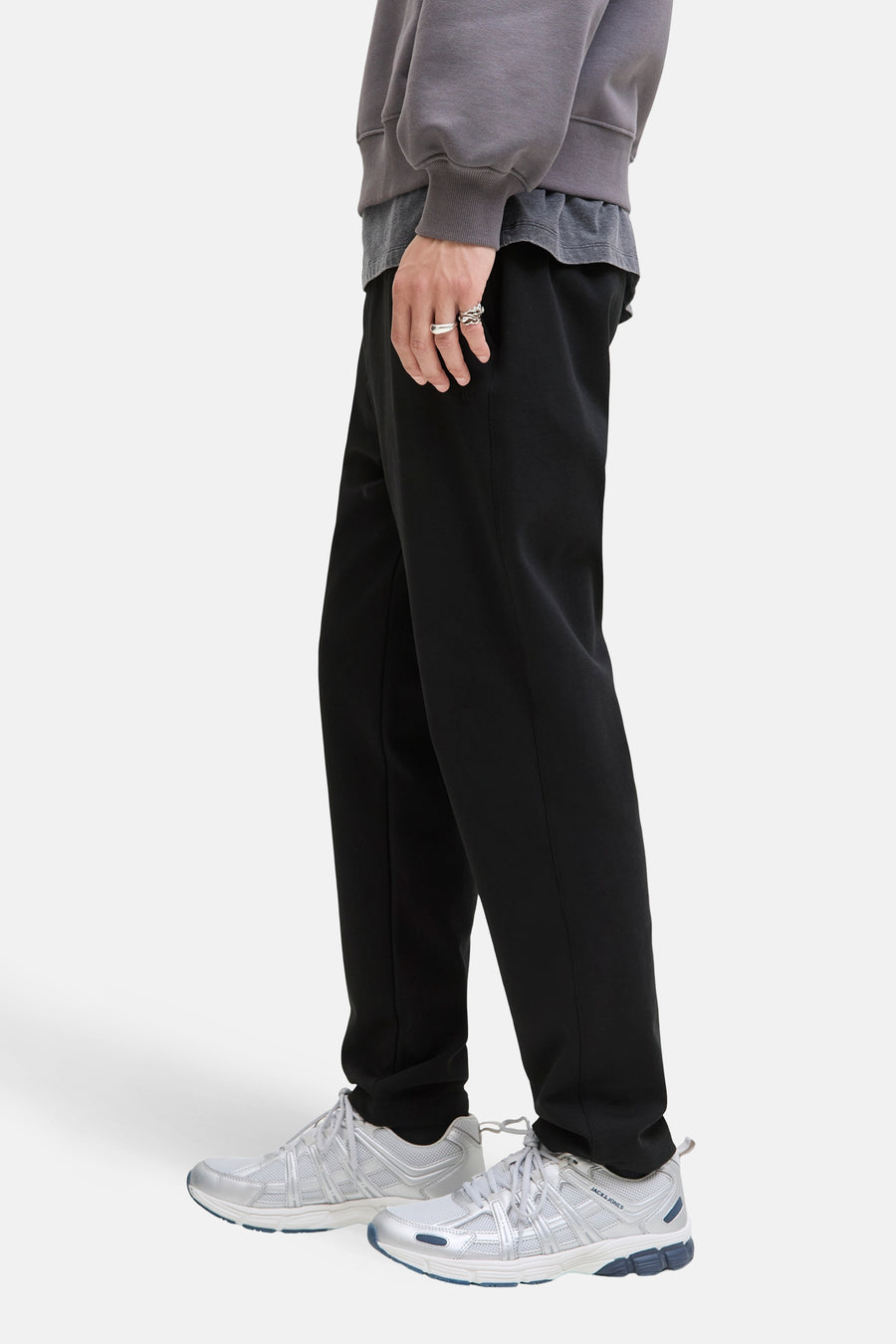 Pantalon noir de JACK & JONES JEANS INTELLIGENCE, avec des baskets argentées et un pull gris, vue de côté.