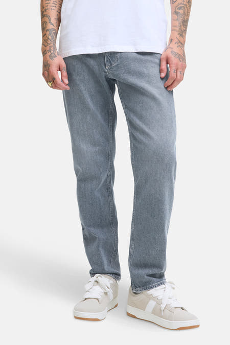 Jean tapered gris clair de JACK & JONES JEANS INTELLIGENCE, associé à des sneakers blanches et un T-shirt blanc.