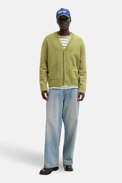Gilet vert de ORIGINALS BY JACK & JONES, porté sur un chemisier rayé avec une casquette bleue et des jeans larges.