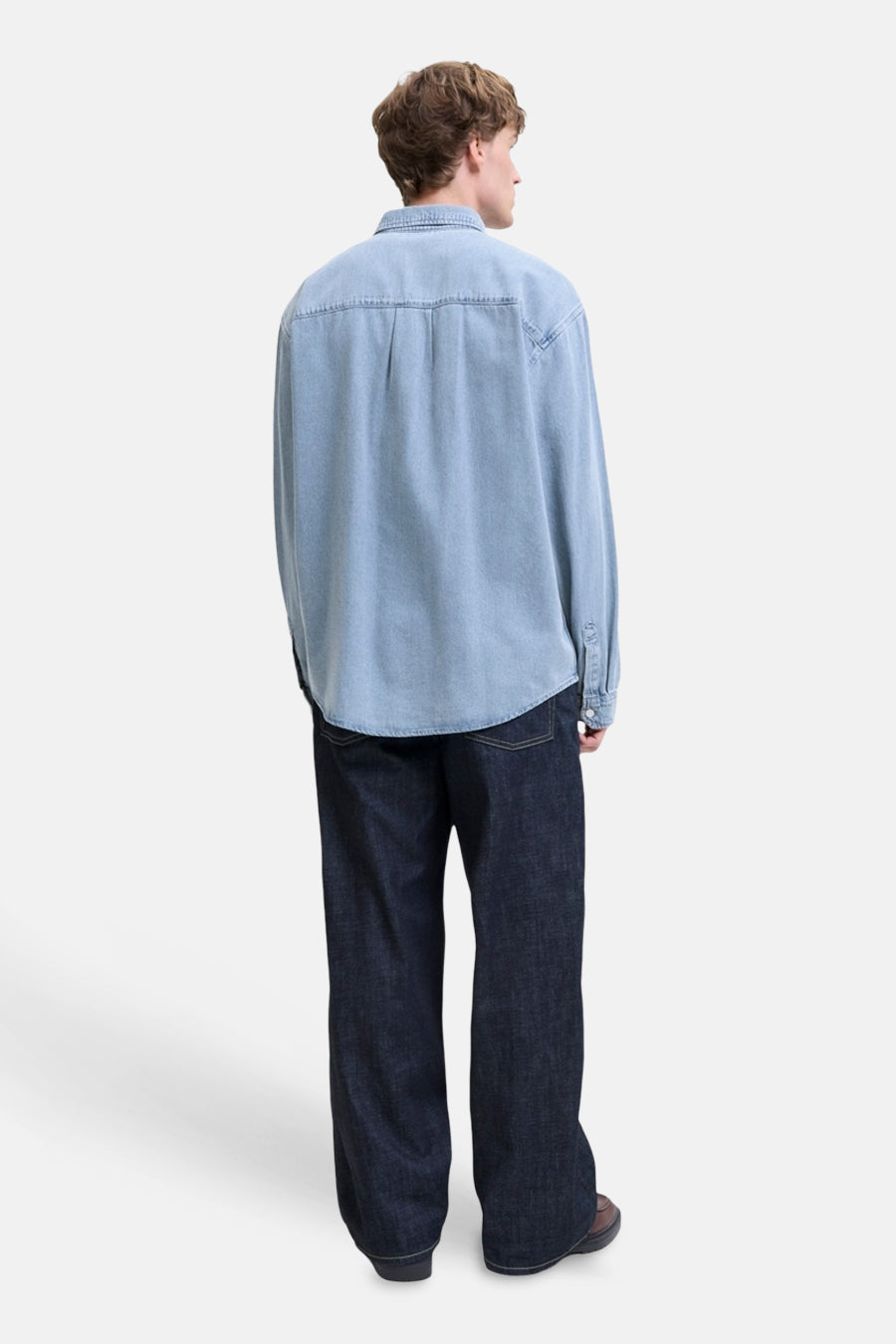 Lichtblauw denim hemd met lange mouwen van ORIGINALS BY JACK & JONES, van achteren gezien, met afgeronde zoom, donkerblauwe jeans en bruine schoenen.