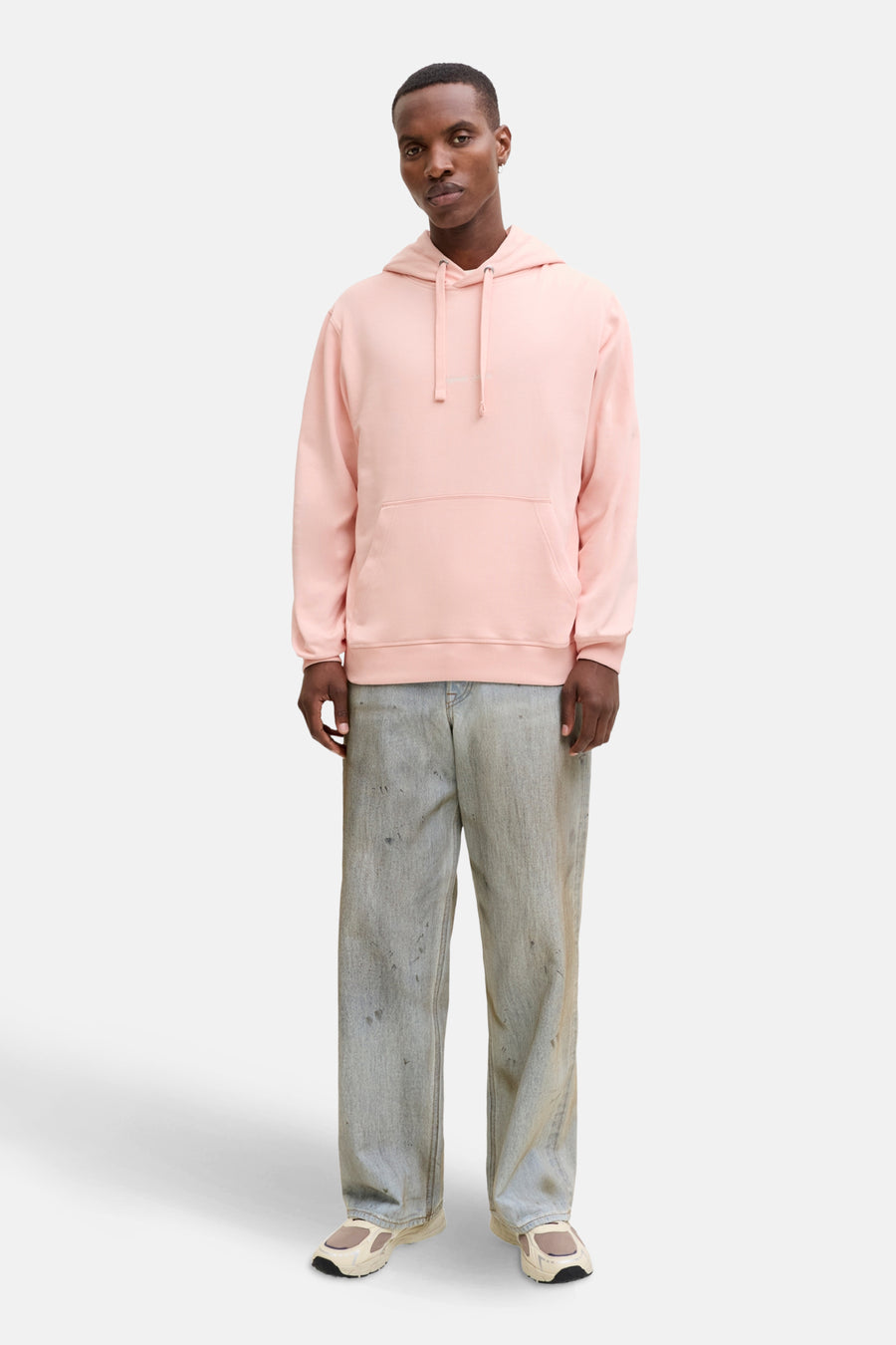 Man in roze hoodie en jeans, staand.