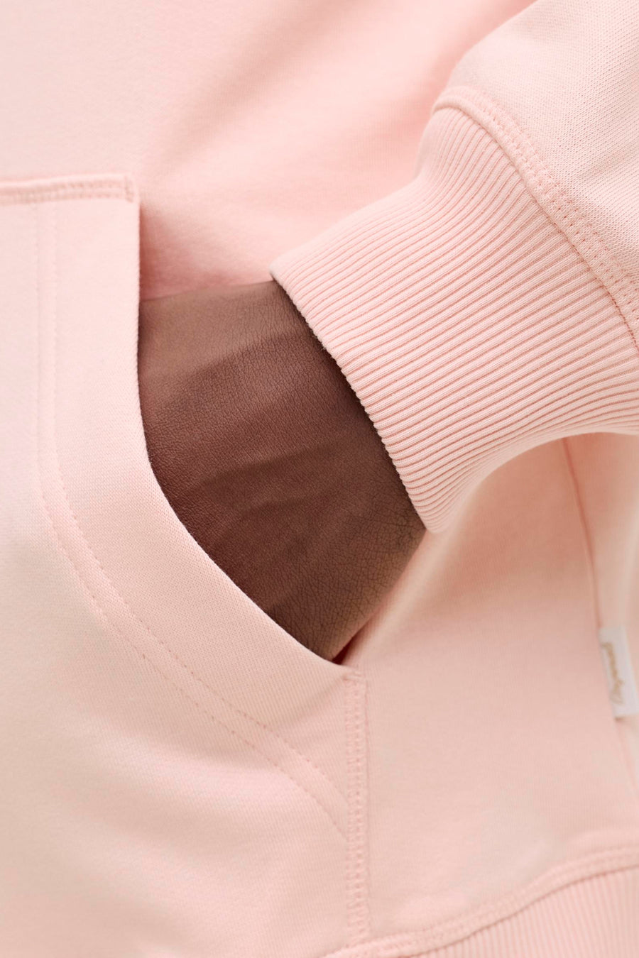 Roze hoodie met ribgebreide manchetten, hand in zak.
