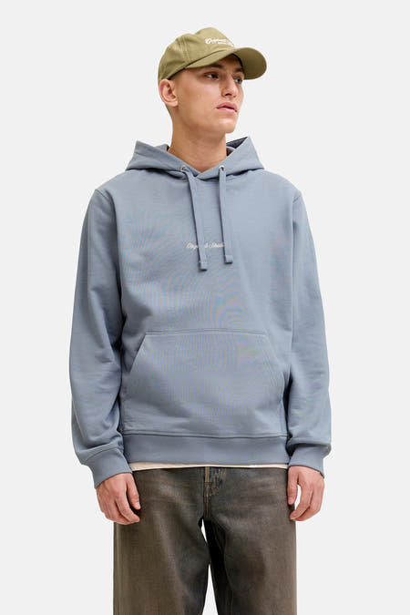 Sweat à capuche bleu de ORIGINALS BY JACK & JONES, porté avec une veste en cuir, un pantalon ample et une casquette.