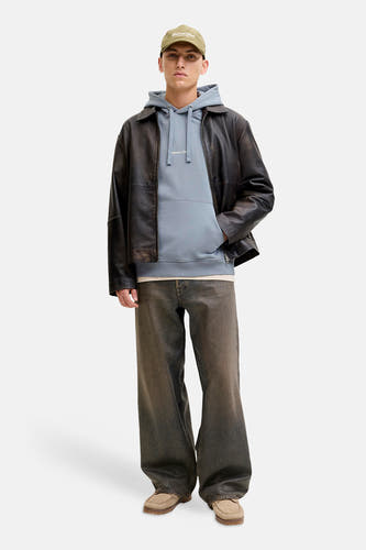 Sweat à capuche bleu de ORIGINALS BY JACK & JONES, avec un imprimé texte léger, porté sous une veste en cuir et un jean ample.