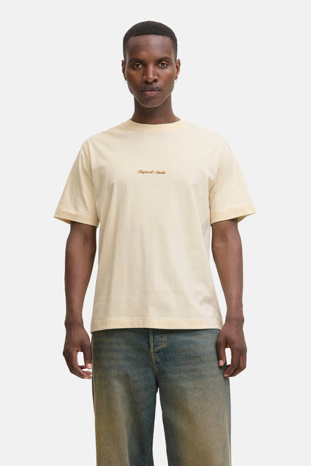 T-shirt beige à manches courtes d'Originals by JACK & JONES, avec un petit logo sur la poitrine et porté avec un jean.