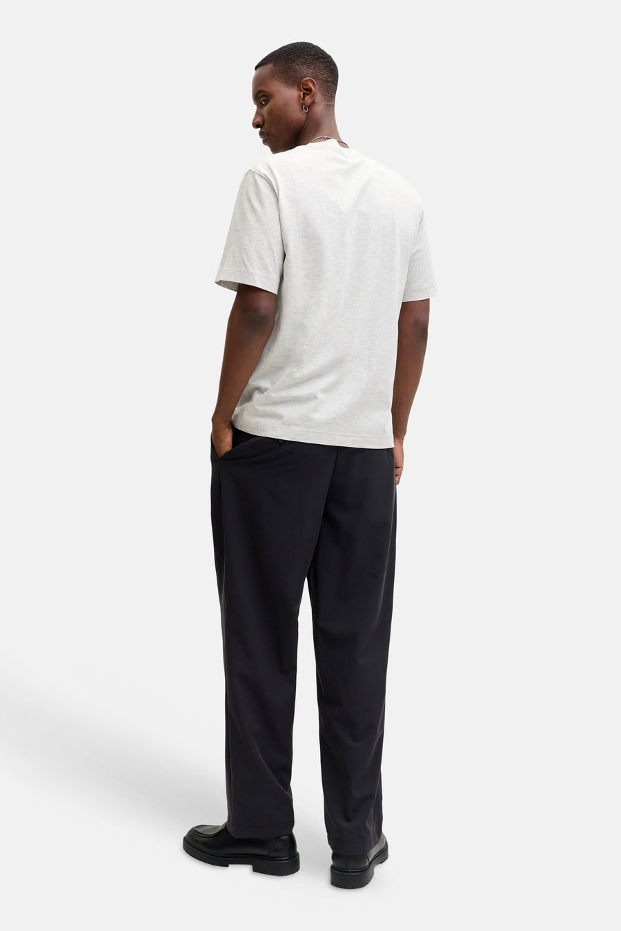 Achterkant van een man met een grijs T-shirt, zwarte broek en schoenen.