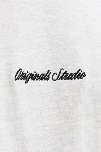 Geborduurd "Originals Studio" op een grijze stoffen achtergrond.
