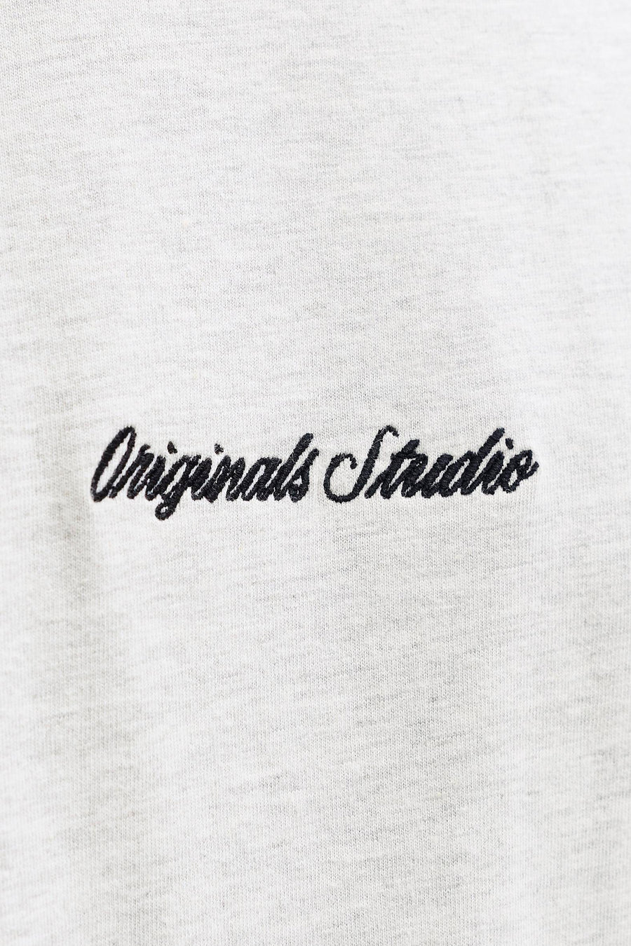 Geborduurd "Originals Studio" op een grijze stoffen achtergrond.
