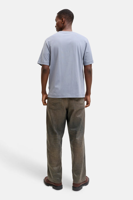 Achterkant van een donkere man in een blauw T-shirt, vuil ogende jeans en bruine schoenen.