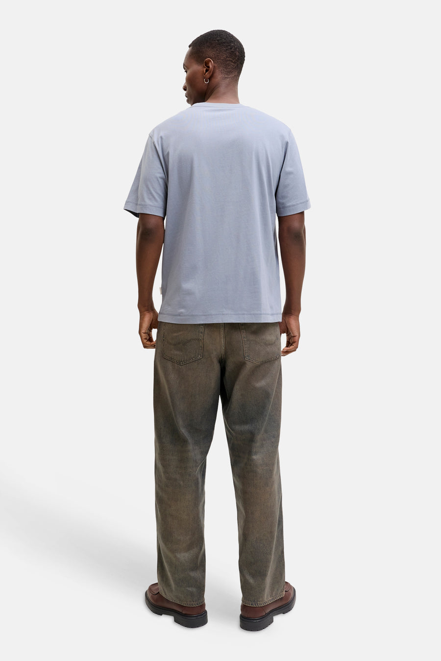 Achterkant van een donkere man in een blauw T-shirt, vuil ogende jeans en bruine schoenen.