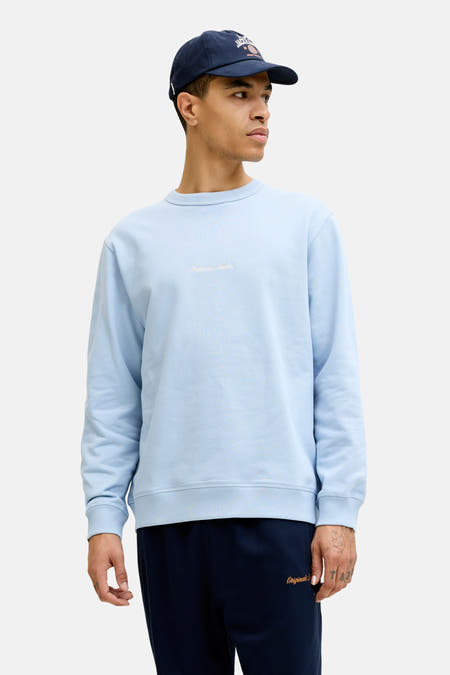 Pull bleu clair de ORIGINALS BY JACK & JONES avec col rond et broderie de texte subtile, porté sous une veste verte à capuche.
