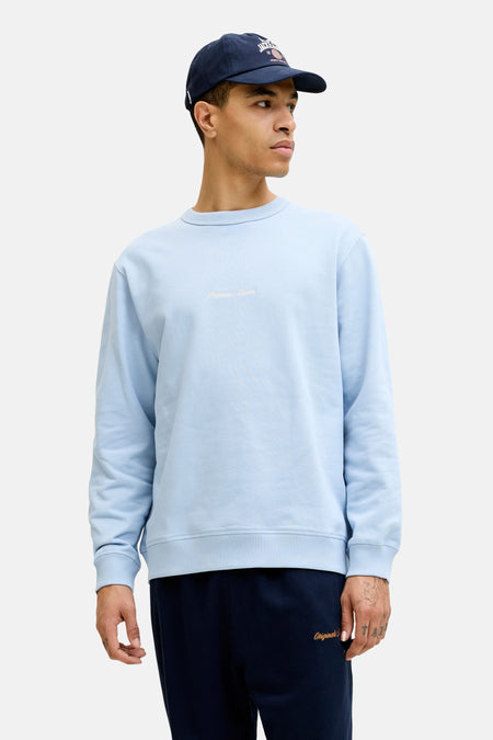 Pull bleu clair de ORIGINALS BY JACK & JONES avec col rond et broderie de texte subtile, porté sous une veste verte à capuche.