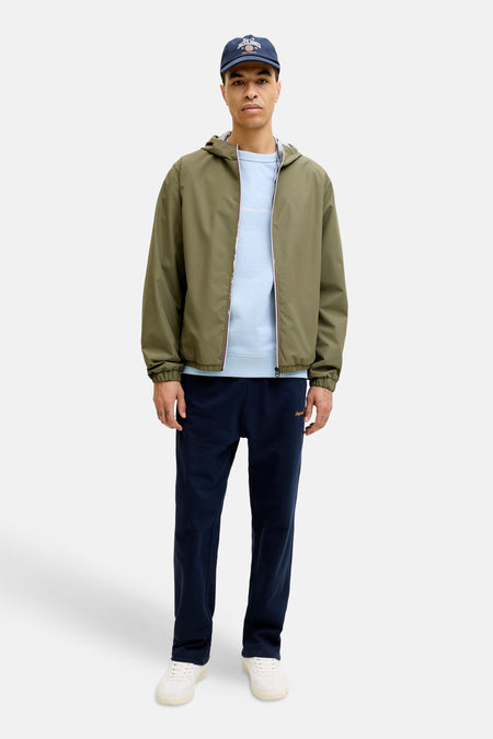 Lichtblauwe sweater van ORIGINALS BY JACK & JONES met ronde hals en subtiel tekstborduurwerk, gedragen onder een groen jack met capuchon.