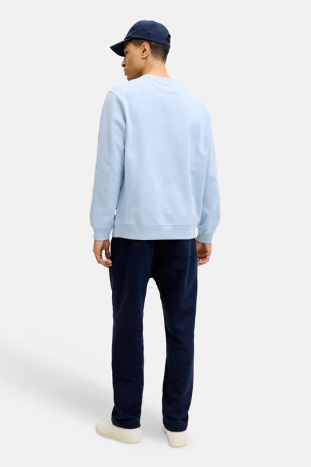Pull bleu clair à col rond de ORIGINALS BY JACK & JONES, avec bords et ourlet côtelés, dos visible sur un homme portant un jogging bleu foncé et une casquette.