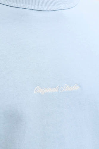 Pull bleu clair à col rond de ORIGINALS BY JACK & JONES avec inscription brodée blanche 'Originals Studio' sur la poitrine.