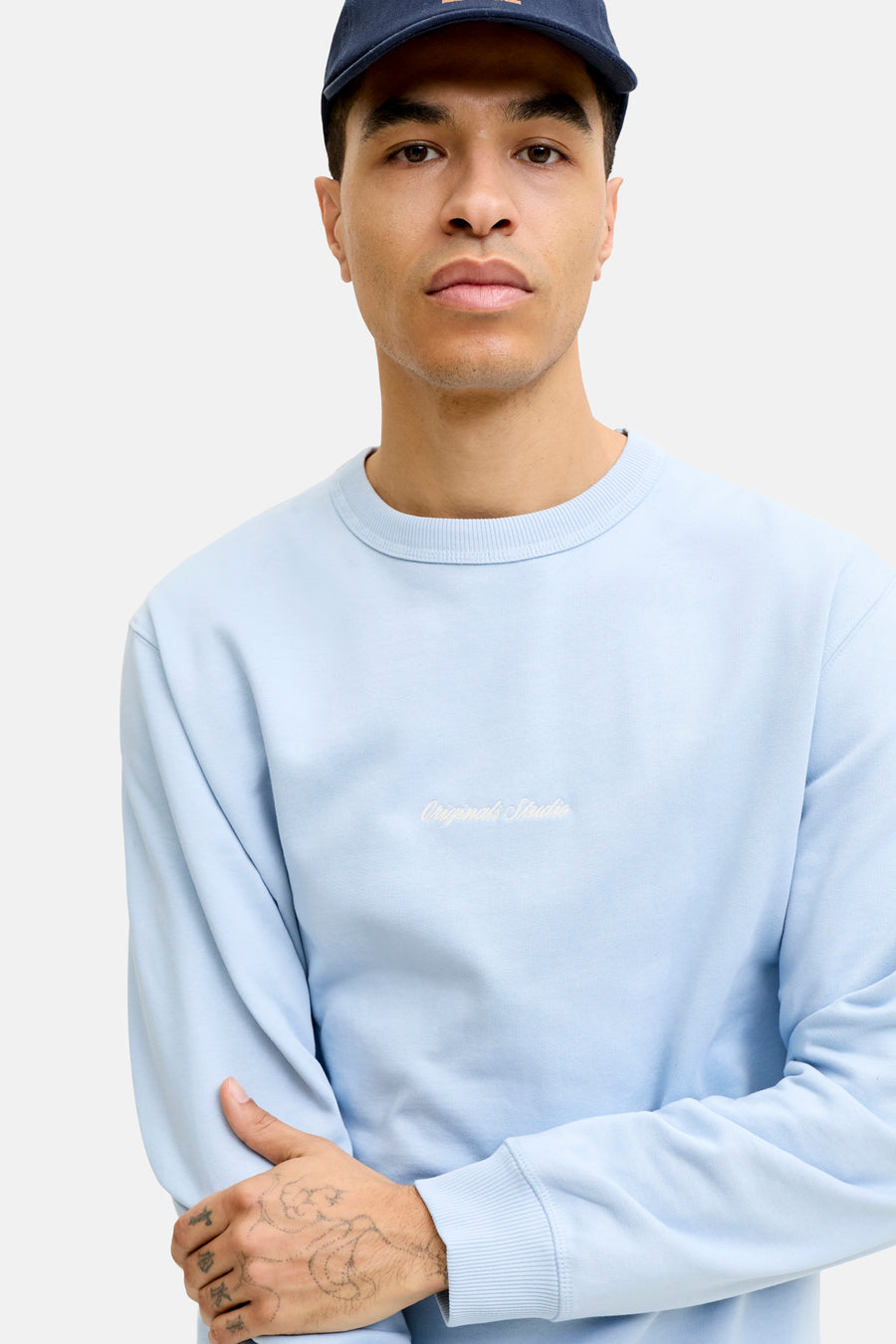 Pull bleu clair à col rond de ORIGINALS BY JACK & JONES, avec inscription brodée blanche 'Originals Studio' sur la poitrine.