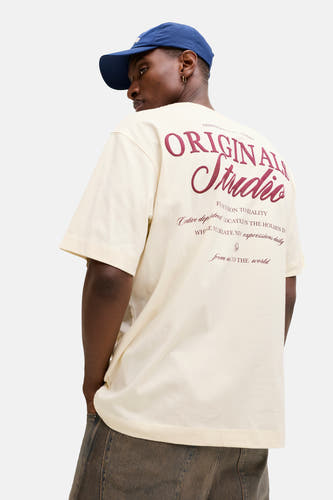 T-shirt écru à manches courtes de Originals by Jack & Jones, avec un imprimé graphique au dos, associé à une casquette bleue et un jean foncé.