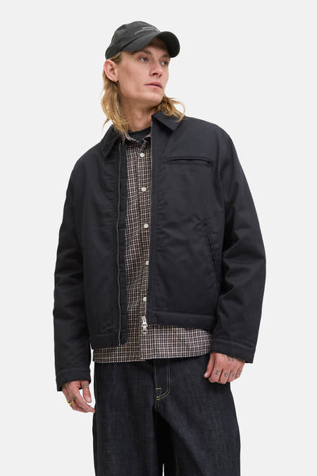 Manteau court noir d'ORIGINALS BY JACK & JONES, porté sur une chemise à carreaux et des jeans foncés avec un casque.