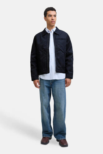 Manteau court bleu d'ORIGINALS BY JACK & JONES, porté sur un chemisier bleu clair et des jeans larges et des chaussures marron.