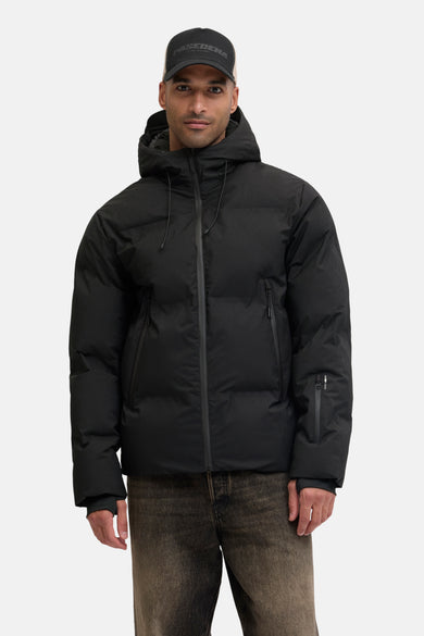 Manteau noir court de CORE BY JACK & JONES, avec capuche et fermeture éclair, associé à un chapeau et des jeans.