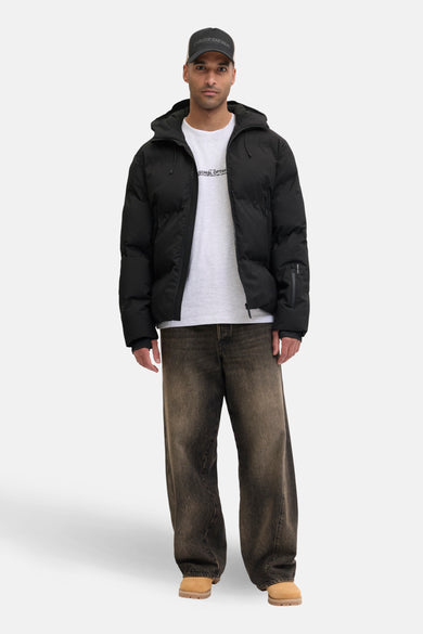 Manteau court noir de CORE BY JACK & JONES, porté avec un T-shirt blanc et des jeans marrons.