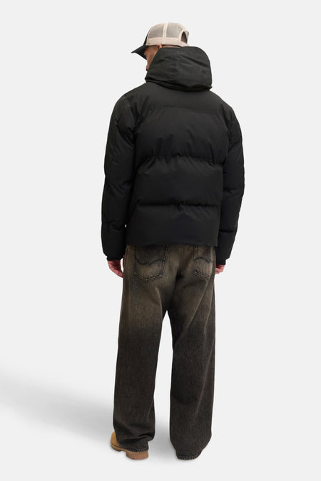 Manteau noir court de CORE BY JACK & JONES, avec un capuchon et associé à des jeans décontractés et des chaussures en cuir de mouton.