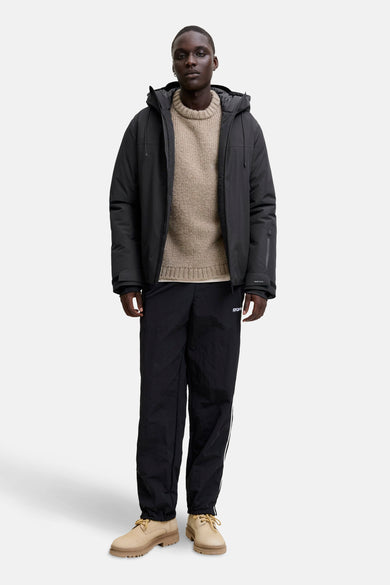 Manteau court noir de CORE BY JACK & JONES, avec capuche et porté avec un pull et un pantalon de jogging.