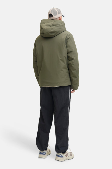 Veste courte verte de CORE BY JACK & JONES, portée de dos avec capuche, casquette de camionneur, pantalon noir à rayures et baskets.