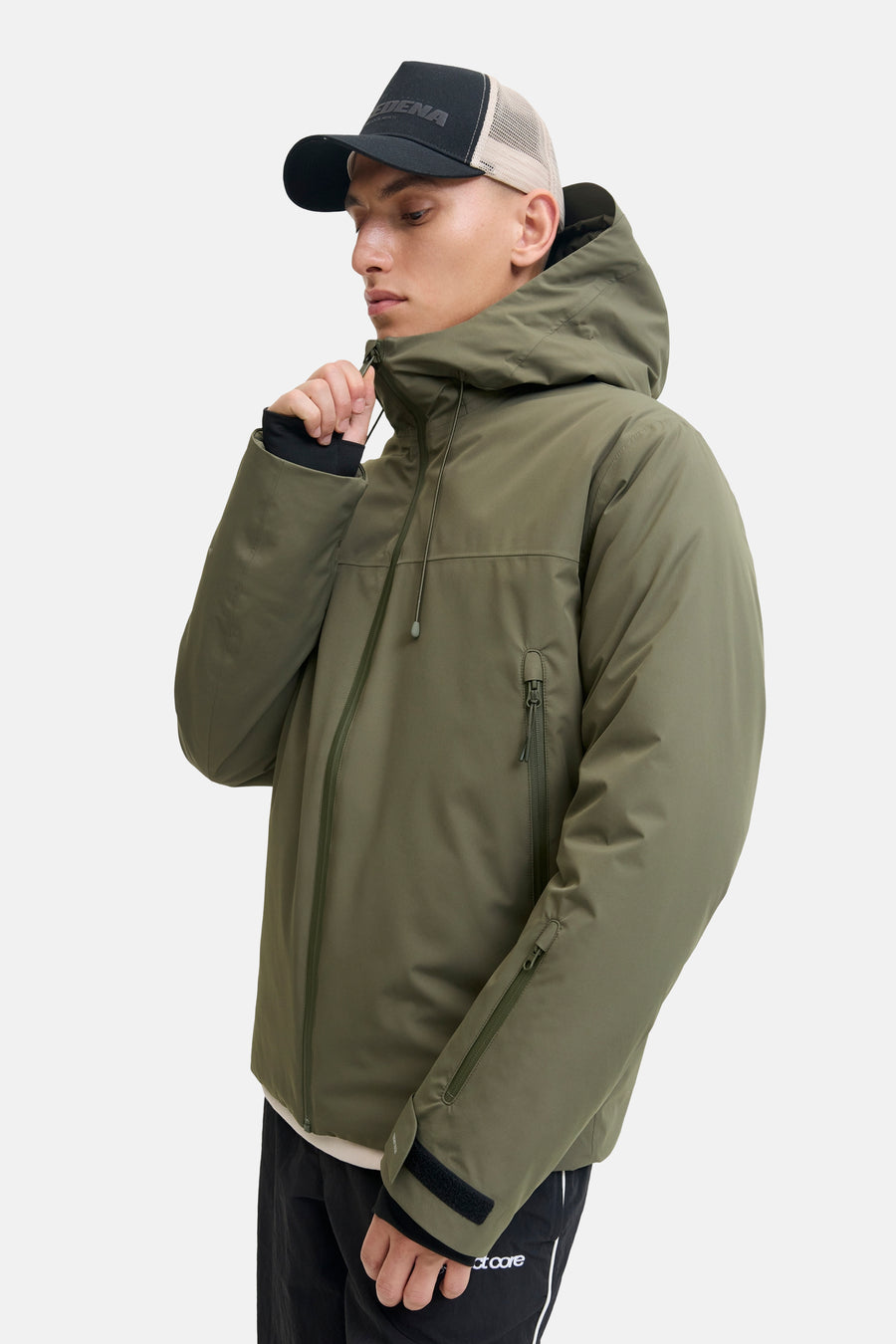 Veste courte verte de CORE BY JACK & JONES avec capuche, fermetures éclair et fermetures velcro, portée par un mannequin avec casquette.