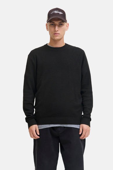Sweat-shirt noir à col rond de CORE BY JACK & JONES, porté avec un chapeau de baseball et une chemise rayée.